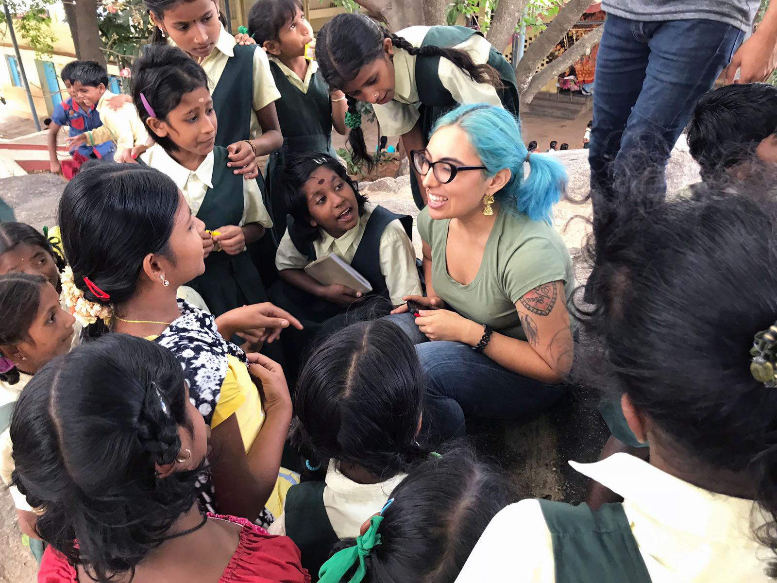 微笑的足彩外围网站学生坐在地上，周围是倾听的年轻学生在印度.